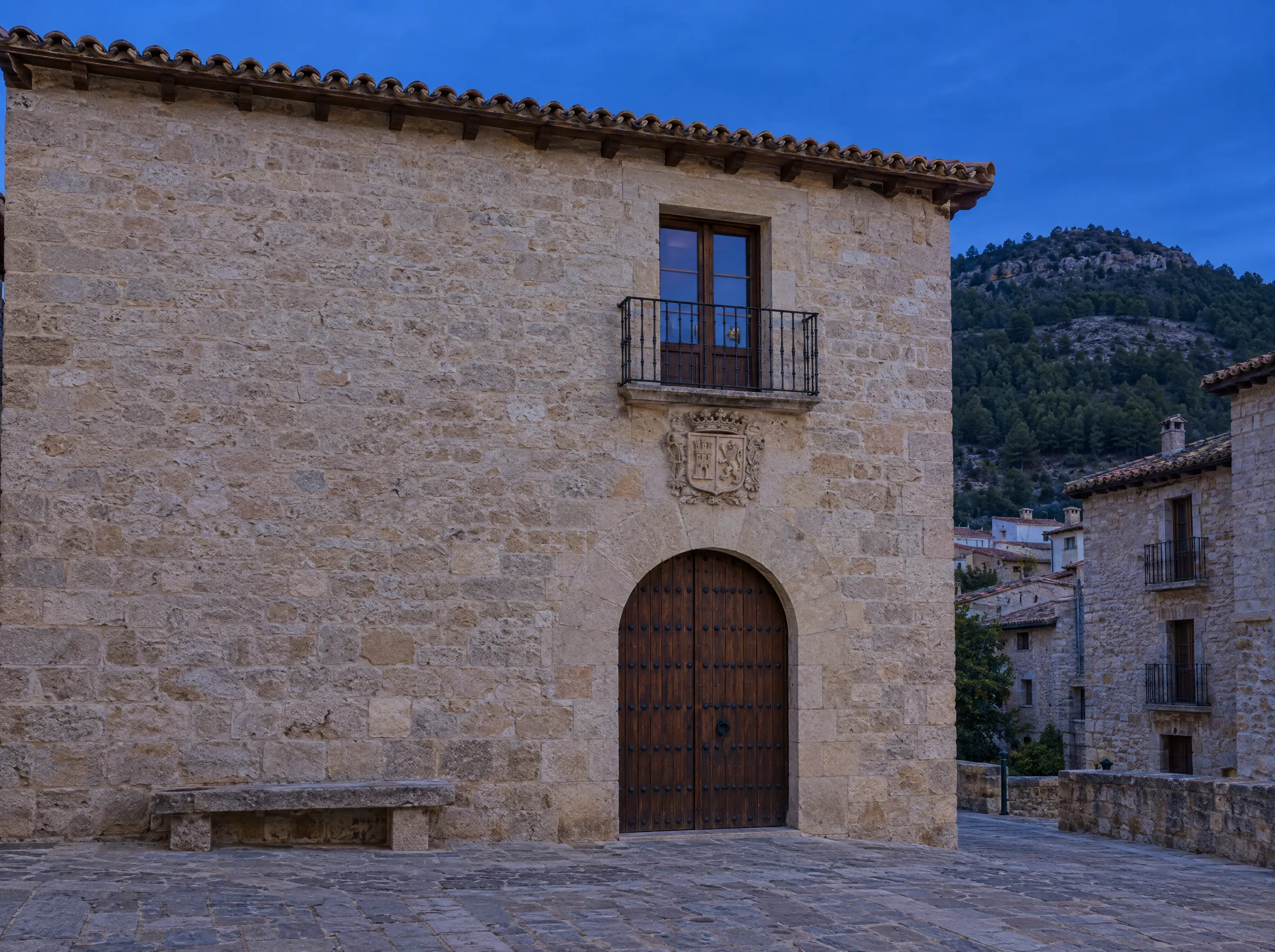 Fachada de piedra de una casa consistorial de pueblo al anochecer, con puerta de madera en arco